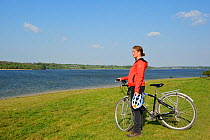 Young woman cycling around Rutland Water, stopping to admire the view, Rutland, UK, April 2011, Model released.