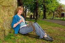 Woman leaning against tree, feeding Grey Squirrel (Sciurus carolinensis) in parkland, Regent's Park, London, UK, April 2011, Model released.