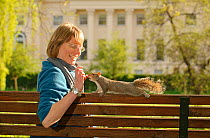 Woman sitting on bench, feeding Grey Squirrel (Sciurus carolinensis) in parkland, Regent's Park, London, UK, April 2011, Model released.