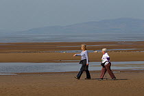 Two women walking along sandy beach at low tide, near Maryport, Solway Firth, Cumbria,UK, April 2011