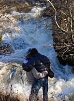 Rear view of couple watching leaping salmon. River Marteg SSSI, Gilfach farm nature reserve, Radnorshire Wildlife Trust, November. Model released