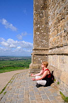 Woman meditating by the 15th century church St. Michael's Tower at the summit of Glastonbury Tor, Somerset, England, May. Model released