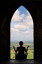 Woman meditating by the 15th century church St. Michael's Tower at the summit of Glastonbury Tor, Somerset, England, May. Model released