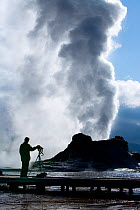 Photographer lined up on boardwalk to photograph Castle Geyser at Old Faithful geothermal area, dawn, Yellowstone National Park, Wyoming, USA, September 2008