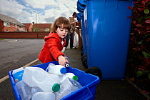 Young girl and mother recycling plastic and cardboard in street, Derbyshire, UK, April, Model released
