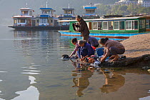 Women washing clothes next to tourist boats at the shore of the Li River. Yangshuo, Guangxi, China, November.