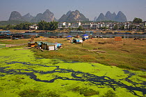 Polluted tributary of the Li River with town and mountains on the horizon. Yangshuo, Guangxi, China, November 2006.