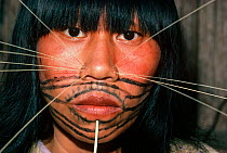 Red and black paint covers a Matses woman's face, and she wears decorative spines on both sides of her nose. This makeup represents the whiskers of the jaguar spirit. Amazon, Peru, November 2005.