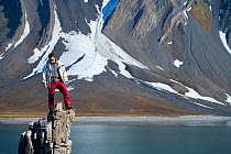 Field Assistant, Jason Roberts, standing on top of rock pinnacle, Svalbard, Spitzbergen, Norway, July 2009, Taken on location for the BBC series, Frozen Planet.