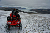 Cameraman, Mark Smith, on an all-terrain-vehicle searching for Arctic wolves, Ellesmere Island, Nunavut, Canada, June 2008. Taken on location for the BBC series, Frozen Planet.