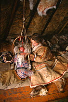 Nenets woman comforting baby inside Reindeer skin tent. Yamal, Siberia, 1996. 40 BELOW bookplate.