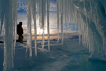 Person standing infront of long icicles, outside volcanic ice cave, Mount Erebus, Antarctica. Taken on location for BBC Frozen Planet series, 2009