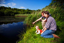 Family sitting beside water watching wildlife at Westhay SWT reserve, Somerset Levels, Somerset, England, UK, June 2011 Model released