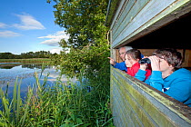 Family, man, girl and boy, birdwatching from hide at Westhay SWT reserve, Somerset Levels, Somerset, England, UK, June 2011 Model released