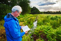 Man using ID handbook at Westhay SWT reserve, Somerset Levels, Somerset, England, UK, June 2011 Model released