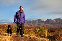 Man walking with dog along footpath through young Scots pine trees, Little Assynt Estate, near Lochinver, Assynt, Sutherland, NW Scotland, UK, January 2011, Model released. 2020VISION Exhibition. 2020...