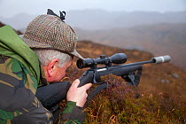 Deer stalker looking through telescopic lens of gun, deer stalking, Assynt Foundation, Glencansip Estate, Assynt, Sutherland, Scotland, January 2011. Model released