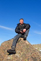 Photographer Peter Cairns sitting on glacial rock, Coire Lochain, Cairngorm Mountains, Cairngorms NP, Highland, Scotland, UK, February 2011. Model released