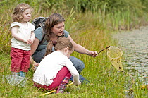Children and mother pond dipping and enjoying pond environment at Little Bradley Ponds, Bovey Tracy, Devon, UK. July 2011. Model released.