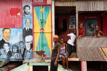 Young people selling barbequed corn at roadside stand decorated with colourful portraits of famous men. Gouyave, Grenada, West-Indies, Caribbean, May 2005. No release.