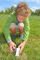 Child in garden collecting insects in jam jar. France, Europe, August. Model released.