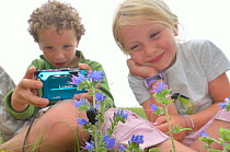 Children in garden photographing flowers and insects. France, Europe, August. Model released.