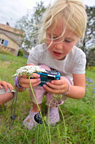 Child in garden photographing flowers and insects. France, Europe, August. Model released.