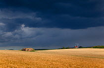 Storm clouds over field after harvest with WWII pillbox and windmill in distance , Weybourne, Norfolk, UK, July 2011