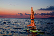 Surf instructor Tara Angioletti does a head stand on her stand-up paddle board. Canoe Bearch, Maui. Hawaii. Model released.