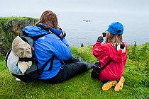 Mother and young girl on cliff photographing Puffin with soft puffin toy in her coat, Lunga, Argyll, Scotland, UK, August 2010, model released