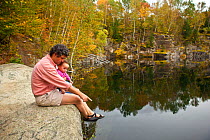 A man and his young daughter sitting on rock next to a pond in an abandoned granite quarry, Millstone Hill, Barre, Vermont, USA. Model released, September 2010