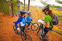 Three women check their map while mountain biking on a trail in an abandoned granite quarry on Millstone Hill, Barre, Vermont, USA. Model released, October 2010