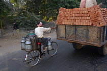Cyclist hitching free ride behind truck carrying bricks on road, Karnataka, Southern India