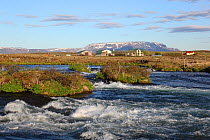 Laxa River from lake Myvatn flowing past a farm with distant mountains, Iceland, June 2009