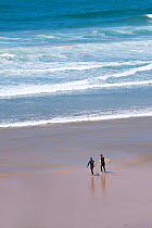Surfers carrying their surfboards down the beach, Fistral Beach, Newquay, Cornwall, UK, July 2011