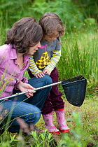 Mother and daughter pond dipping in rhyne, visiting the Westhay Nature Reserve, Somerset Levels, UK, June 2011, model released