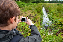 Boy photographing rhyne on family visit to the Westhay Nature Reserve, Somerset Levels,  UK, June 2011, model released
