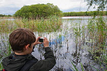 Boy photographing wetlands on family visit to the Westhay Nature Reserve, Somerset Levels, UK, June 2011, model released