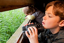Boy birdwatching from  hide on family visit to the Westhay Nature Reserve, Somerset Levels, UK, June 2011, model released