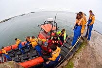 Group of tourists wearing waterproof clothing and life jackets board zodiac boat for tour around Bass Rock, North Berwick, Firth of Forth, Lothian, Scotland, UK, August 2011