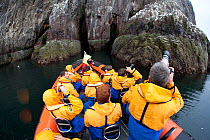Group of tourists wearing waterproof clothing and life jackets photograph seabirds from zodiac boat on tour around Bass Rock, North Berwick, Firth of Forth, Lothian, Scotland, UK, August 2011