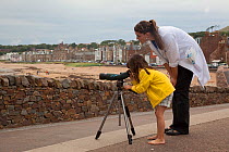Woman helping young girl to look down telescope at seabirds at Scottish Seabird Centre, North Berwick, Firth of Forth, Lothian, Scotland, UK, August 2011