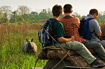 People on an elephant-back safari looking at a Greater One-horned / Indian / Asian One-horned Rhino (Rhinoceros unicornis). Vulnerable. Kasiranga National Park, Assam, India, April.