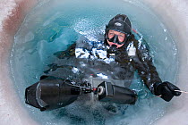 Wildlife cameraman Doug Allan prepares for a dive in hole drilled in sea ice. Ross Sea, McMurdo, Antarctica. Freeze frame book plate page 38.