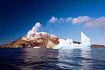 Iceberg floating in front of smoking volcano. Zavadovski Island, South Sandwich group, Antarctica. Freeze Frame book plate page 153.