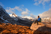 Woman sitting on rock admiring the view during the descent from Tom na Gruagaich, Beinn Alligin, Torridon, Scotland, UK, February 2010 Model Released. Did you know? Beinn Alligin is 260 million years...