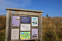 RSPB Wallasea Wild Coast Project sign, with man walking past in background, RSPB Greater Thames Futurescapes Project, Wallasea Island, Essex, England, UK, October 2011