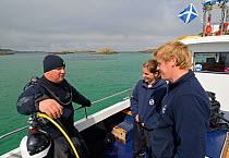 Underwater photographer Alex Mustard on board Sea Life Surveys boat Sula Crion preparing to dive at the Cairns of Coll, watched by two tourist guides, Inner Hebrides, Scotland, UK, July 2011
