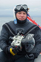 Portrait of underwater photographer Alex Mustard wearing a wetsuit with camera and dome port, Inner Hebrides, Scotland, UK, July 2011