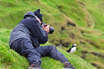 Tourist photographing a puffin (Fratercula arctica), Shetland Isles, Scotland, UK, July 2011
